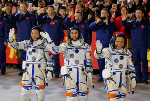 Traja čínski astronauti v bielych skafandroch mávajú davu.