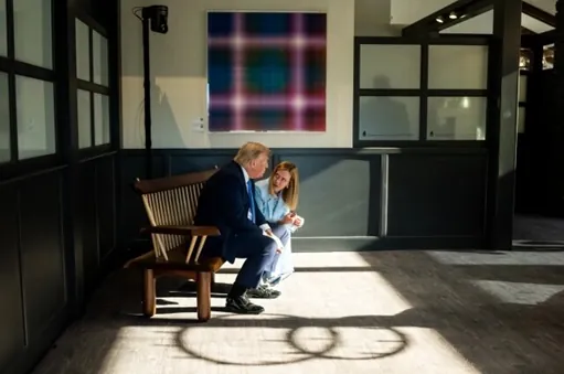 Donald Trump a žena na drevenej lavičke v rozhovore pred obrazom.