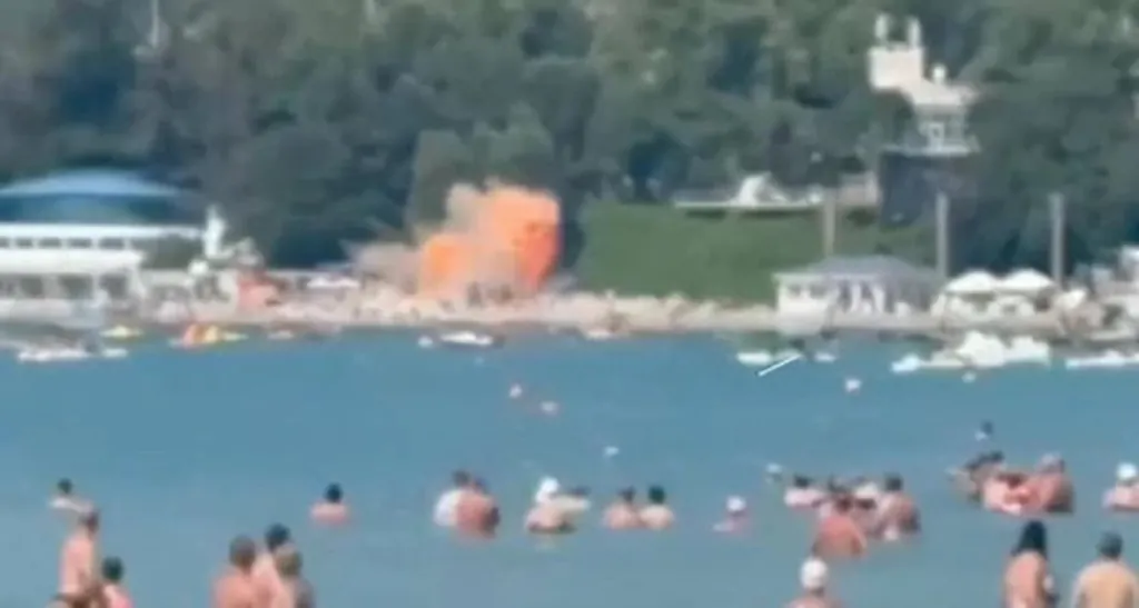 Oranžový výbuch na pláži za ľuďmi kúpajúcimi sa v mori